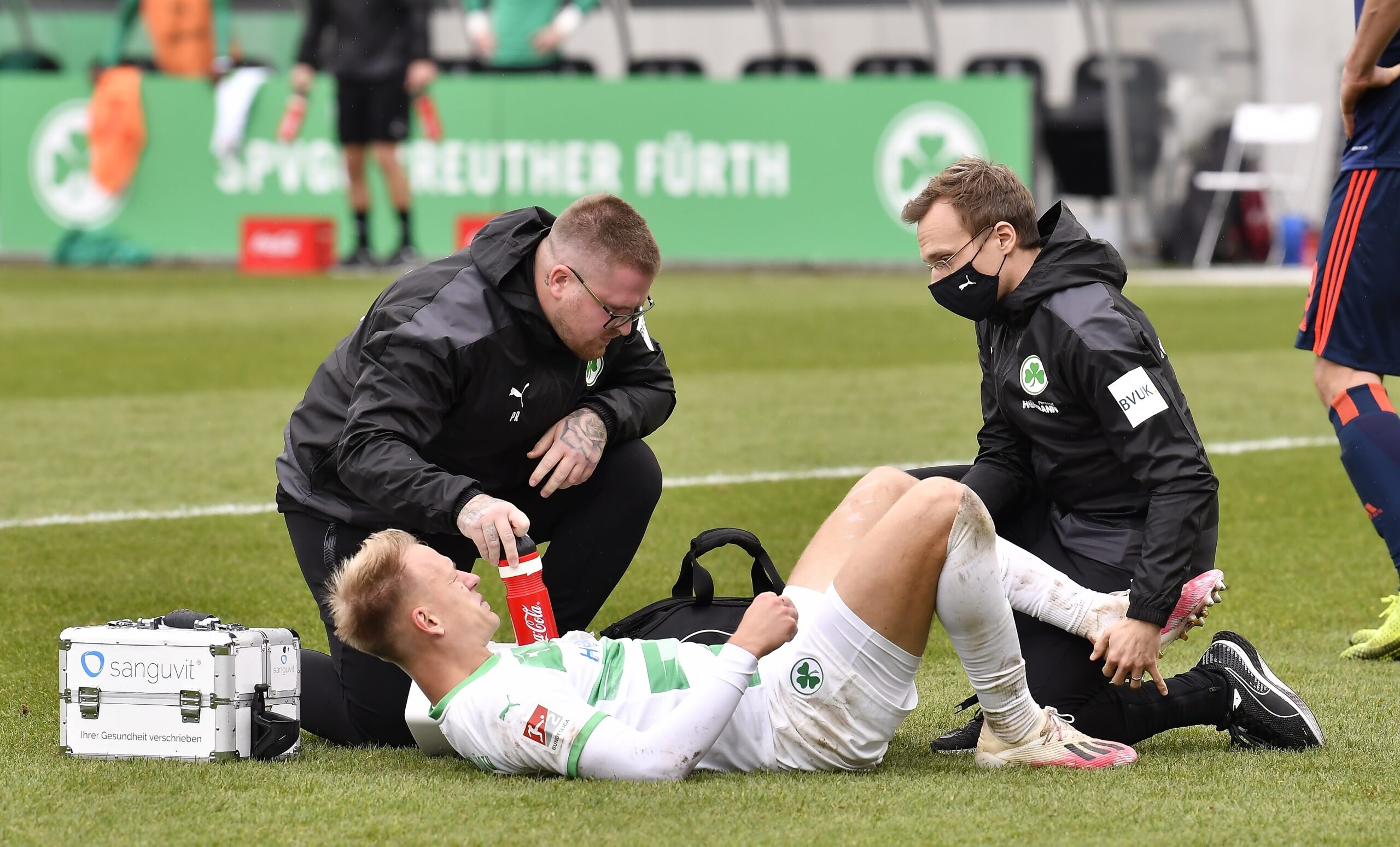 Physiotherapeut Patrick Rutte kniet auf einem Fußballfeld und begleitet einen verletzten Fußballer therapeutisch